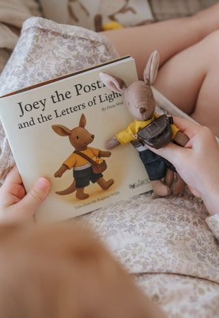 child holding children's book with Rugaroo doll dressed up as a postie