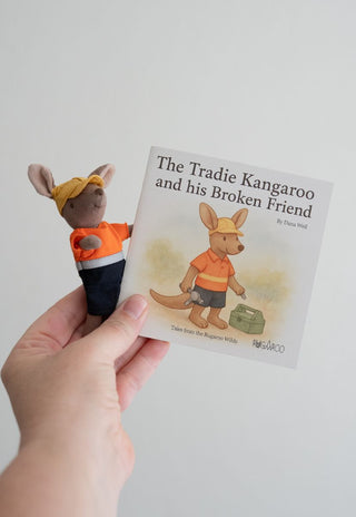 Hand holding a book titled 'The Tradie Kangaroo and his Broken Friend' with a toy kangaroo character.