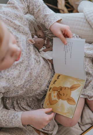 Child reading a book with a rugaroo children's book while holding her Rugaroo dolls