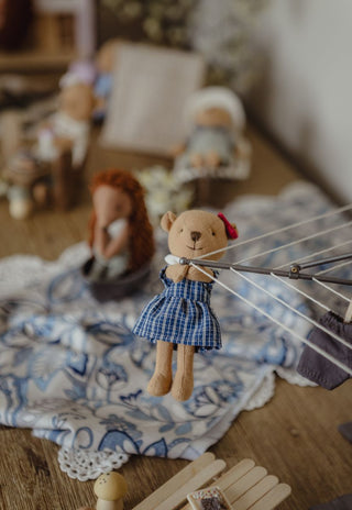 A Rugaroo miniature wombat prep/Kindy doll in a school uniform hangs from a metal clothesline in a softly styled room scene with other dollhouse Australian figure dolls.