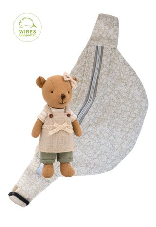 A small plush barista wombat doll wearing a cream apron and green shorts, posed in front of a matching beige floral fabric bum bag with a silver zipper on a white background.