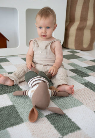 aby sitting on Rugabub green checkered foam baby play mat holding soft toy.