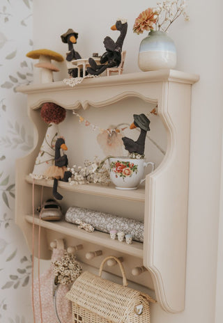 Black swan Rugaroo heirloom dolls displayed on a cream vintage-style nursery shelf with miniature accessories, dried flowers, and a floral teacup