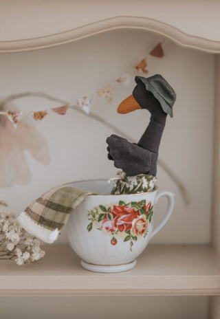 Close-up of Byron the Rugaroo black swan plush doll sitting in a vintage floral tea cup on a nursery shelf - Australian heirloom miniature toy as home decor