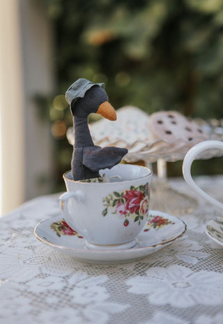 Byron the Sunbaking Black Swan Rugaroo doll wearing his green sun hat, nestled in a vintage floral tea cup; collectible Australian plush toy