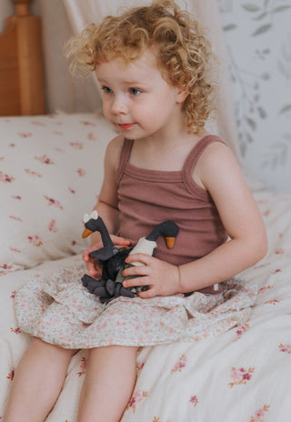 Curly-haired girl cuddling Reed and Maali Rugaroo black swan miniature plush dolls on a floral bed - premium Australian heirloom collectible toys for children