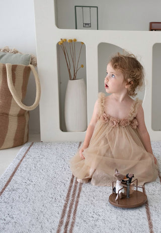 Child sitting on Rugabub Cala neutral striped foam baby play mat.