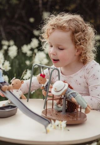 Girl playing with Rugaroo wombat dolls on a miniature playground set