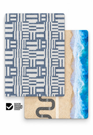 Rugabub Azur / Ocean Road reversible baby play mat showing a blue and white geometric woven rug design on one side and a beach play map with winding road, train track and ocean waves on the other, Good Design Award winner