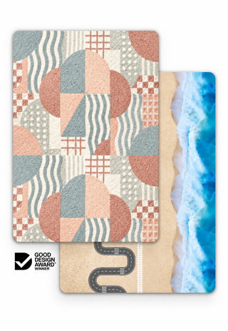 Rugabub Coral / Ocean Road reversible baby play mat showing a coral, blush, sage blue and cream geometric rug design with arches, waves and checkerboard on one side and a beach play map with winding road, train track and ocean waves on the other, Good Design Award winner