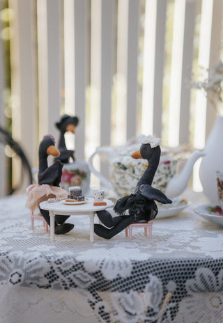 Three black swan Rugaroo Australian animal dolls on a lace-covered veranda table with a miniature tea party set and floral teapot