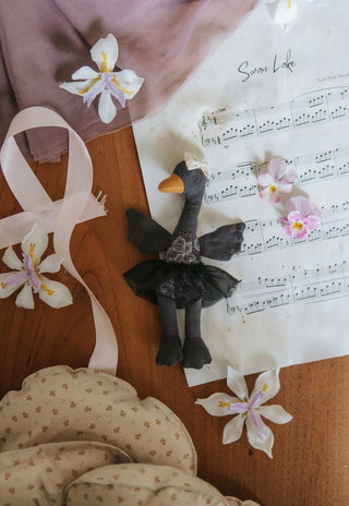 Maali the Opera House Ballerina black swan Rugaroo doll lying on Swan Lake sheet music surrounded by fresh flowers and a floral pouch bag