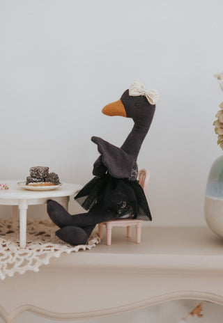 Maali the Opera House Ballerina black swan Rugaroo doll seated at a miniature café table with a tiny lamington and biscuits, styled on a cream surface