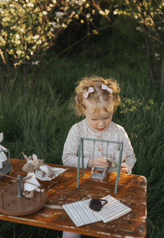 Child sitting at a wooden table outdoors with greenery in the background