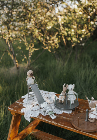 Miniature dolls and playground accessories on a wooden table with a blurred natural background
