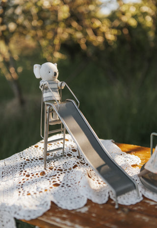 Small toy koala on a miniature slide set on a lace doily with a blurred natural background