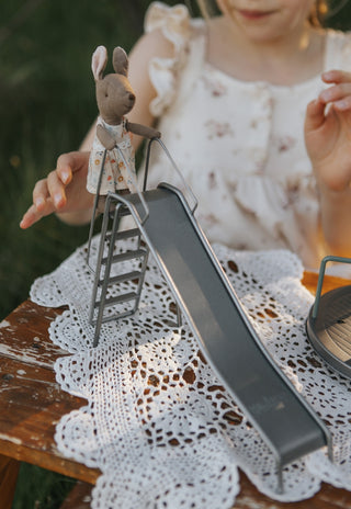 Child playing with a toy kangaroo and ladder of miniature metal slide set on a lace tablecloth