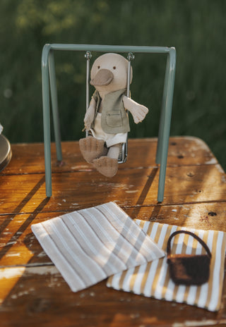 miniature platypus doll on a miniature swing set on a wooden surface with a blurred green background