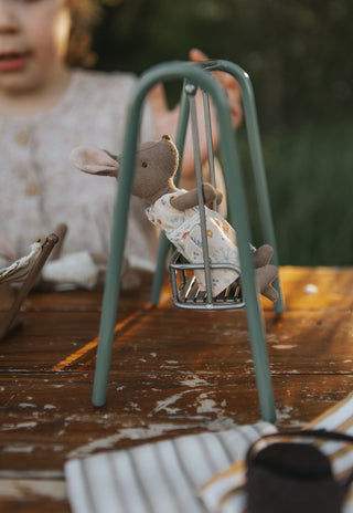 miniature kangaroo doll in a green metal swing on a wooden table with a blurred background