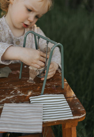 Child playing with a small metal dollhouse swing on a wooden table outdoors