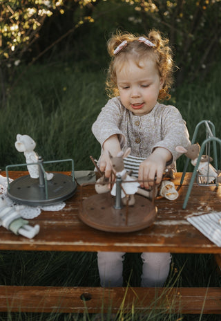 Child playing with toys at a wooden table outdoors