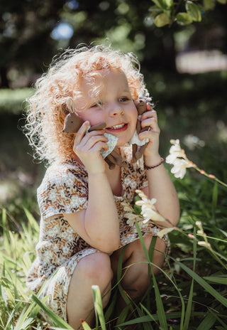 Smiling curly haired child cuddling Mon the Bae and Betty the Bush Belle Rugaroo kangaroo plush dolls to her cheeks in the garden