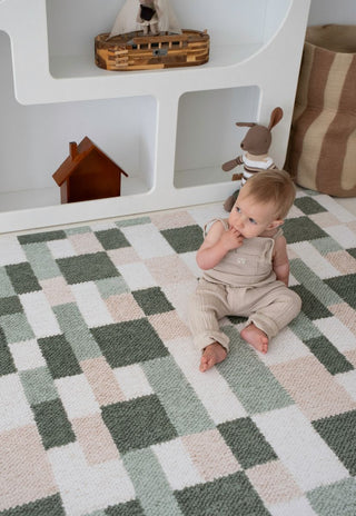 Baby sitting on Rugabub green checkered soft foam baby play mat during play time.