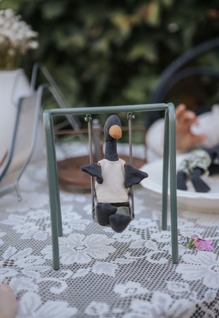 Reed the Wetlands Ranger Rugaroo black swan doll sitting on the miniature swing in cream shirt and khaki pants - Australian heirloom plush toy for small-world play