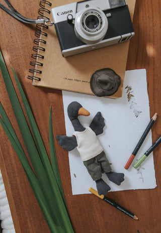 Flatlay of Reed the Wetlands Ranger Rugaroo black swan doll with his ranger hat, sketch pad, vintage camera and wetland reeds - heirloom Australian miniature plush toy