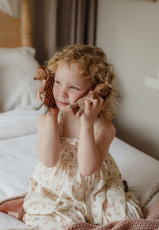 A young child with curly blonde hair sits on a bed, holding Col and Riva the Campground Host Echidnas, Rugaroo miniature dollhouse dolls for kids