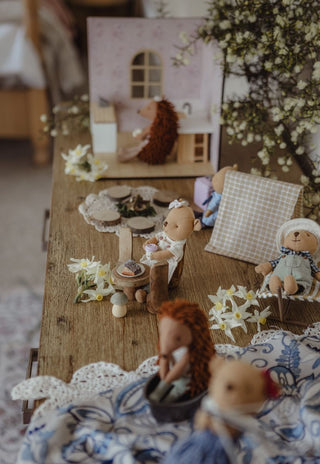 A cozy miniature dollhouse scene on a wooden table, featuring rugaroo miniature australian character dolls