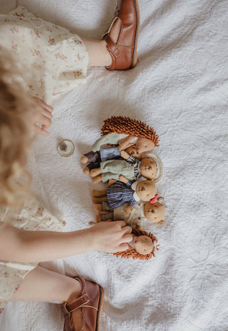 A top-down view of a child's hands and legs interacting with a Rugaroo miniature Australian animal dolls like echidnas and wombats.