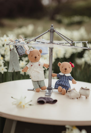 A miniature dollhouse-style scene with two rugaroo wombat dolls beside a small metal clothesline. Marg the wombat Barista, and Maisie the wombat in a school uniform.