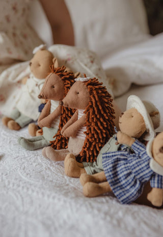 A group of soft, handmade plush echidna and wombat toys arranged on a white textured blanket in a cozy indoor setting.