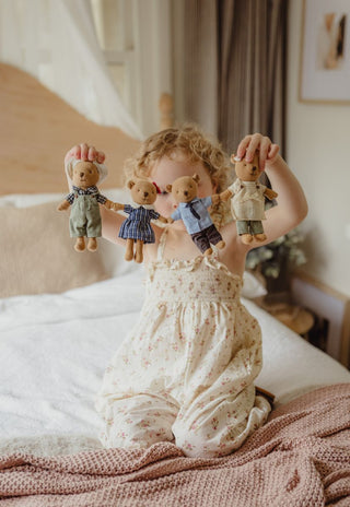 A young child sitting on a bed in a softly lit bedroom, holding four miniature Australian Rugaroo Wombat dolls