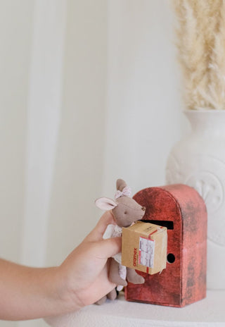 Small stuffed kangaroo doll with a box being held by a hand next to a red mailbox.