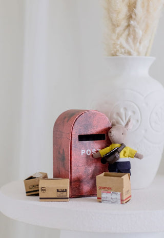 Small toy figure of a kangaroo with an Australian Postman Uniform standing next to a red mailbox on a white surface.