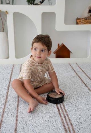 Toddler sitting and playing on Rugabub Cala neutral striped foam baby play mat.
