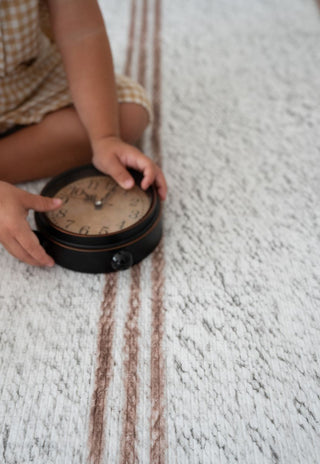 Top view of child sitting on Rugabub Cala neutral striped padded foam baby play mat.