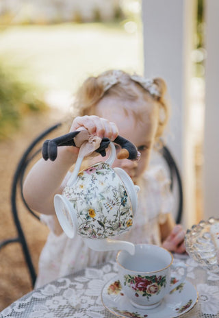 Young girl holding Wattle the Rugaroo black swan plush doll while pretend pouring tea at a garden party - imaginative play with Australian heirloom miniature toy
