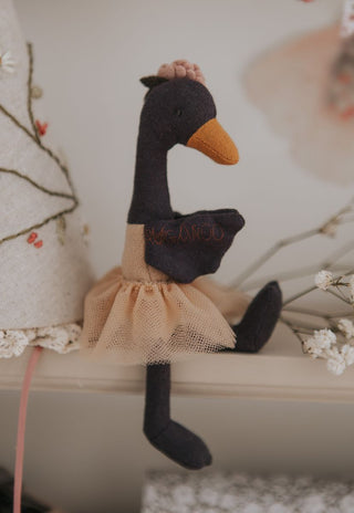 Close-up of Wattle the Bush Florist Rugaroo black swan doll with pink flower crown sitting on a display shelf - Australian heirloom plush toy as nursery decor